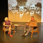 A woman interviewer, Liz Jerrard, seated on a stage with Jon Cruddas MP with a photographic backdrop of Ramsey MacDonald and comrades.